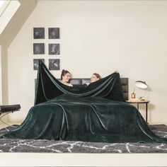 two people laying on a bed covered with a blanket in the middle of a room