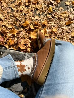 a person's feet with brown and white socks on sitting in the fall leaves