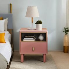 a nightstand with a lamp on top of it next to a bed in a bedroom