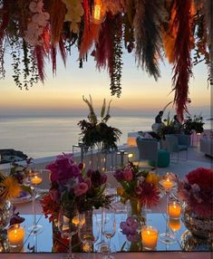 an outdoor dining area with candles and flowers on the table, overlooking the ocean at dusk