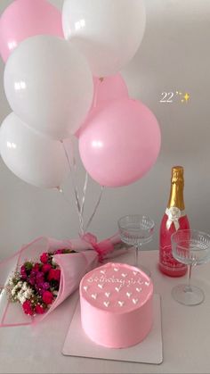 a table topped with pink and white balloons next to a bottle of champagne, cake and flowers