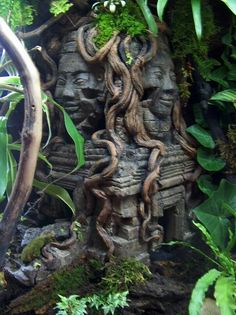 a statue with vines growing out of it's face in the middle of some plants