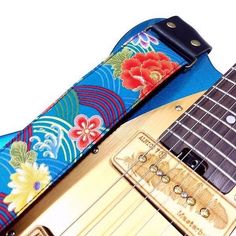 a guitar strap with flowers on it and a blue guitar in the foreground, against a white background