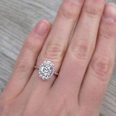 a woman's hand with a diamond ring on top of her finger, next to a wooden table