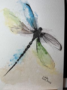 a watercolor painting of a dragonfly on white paper with blue, green and yellow colors