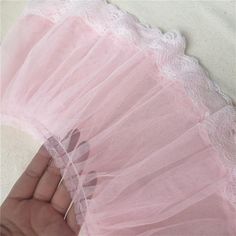 a hand holding a pink lace and tulle fan on top of a white surface