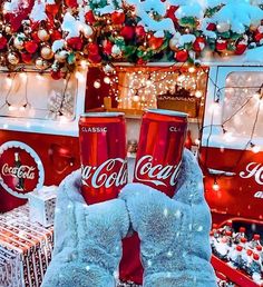 two coca cola cans sitting on top of snow covered ground in front of christmas decorations