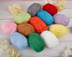 multicolored balls of yarn sitting on top of a white wooden table next to flowers