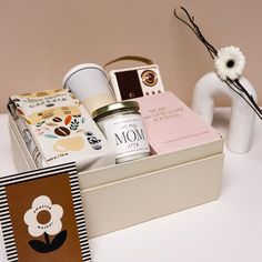 a white vase with flowers and other items in it next to a card box on a table