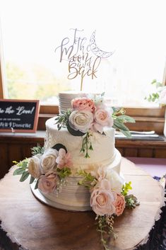 a wedding cake with flowers on top sitting on a table in front of a window