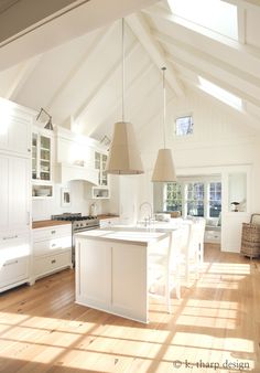 an open kitchen with white cabinets and wood flooring is shown in this image, there are two pendant lights hanging from the ceiling