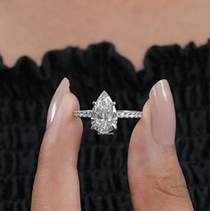 a woman's hand holding an engagement ring in front of her face, with the diamond setting on it