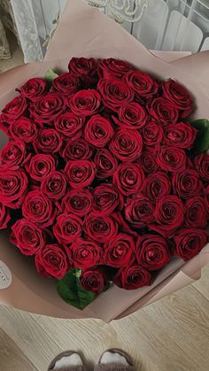 a large bouquet of red roses in a paper box with someone's feet next to it