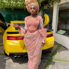 a woman standing next to a yellow car wearing a pink dress and headpieces