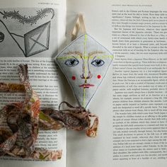 an open book with two origami faces on it and some ribbons hanging from the pages