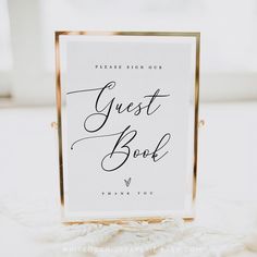 a guest book sign sitting on top of a white tablecloth covered table with gold trim