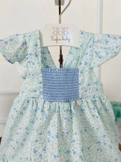 Blue Floral Smocked Dress Girl's traditional floral dress with ruffle hem. Handmade in lightweight cotton, the bodice is beautifully hand-smocked with a butterfly sleeve and big blue gingham bow. Adjustable straps 100% cotton For best results, warm cold or warm water and lay flat/hang to dry Made in Brazil Brand: Kafka Baby SKU: KAF39215 Spring Smocked Dress With Flutter Sleeves, Spring Smocked Dress With Flutter Sleeves And Smocked Bodice, Summer Cotton Smocked Dress With Flutter Sleeves, Flutter Sleeve Smocked Dress With Ruffles For Garden Party, Garden Party Smocked Dress With Ruffle Sleeves, Cotton Smocked Dress With Ruffle Hem For Spring, Spring Cotton Smocked Dress With Ruffle Hem, Spring Cotton Smocked Dress With Ruffles, Cute Gingham Smocked Dress With Ruffles