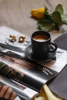 a cup of coffee sitting on top of a magazine next to a pair of gold rings