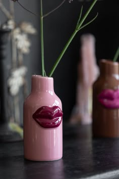 three vases with lipstick painted on them are sitting on a table next to flowers