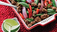 a dish with meat, peppers and onions on a red cloth next to a lime wedge