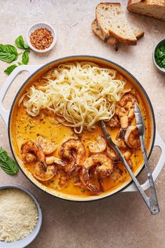 a pan filled with pasta and shrimp on top of a table next to some bread