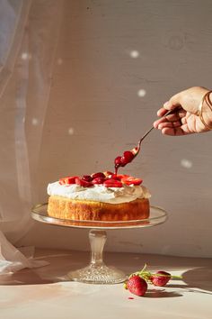 someone is cutting into a cake with strawberries on it