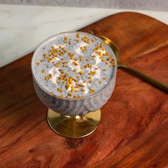 a dessert in a glass on top of a wooden board next to a gold spoon