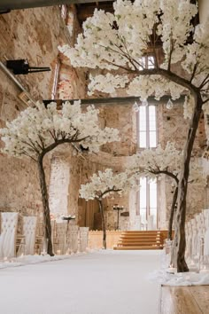 an indoor ceremony with white flowers and trees in the center, surrounded by stone walls