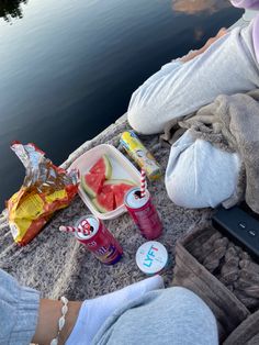 a woman sitting on the edge of a lake with her feet propped up next to food