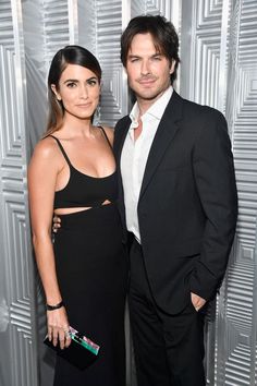 a man and woman standing next to each other in front of a silver wall with squares on it