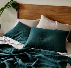 a bed with green linens and pillows on top of it, next to a potted plant