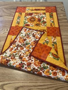 a quilted table runner with sunflowers and polka dots on the edges, sitting on a wooden surface