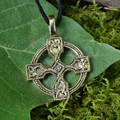 a cross pendant is sitting on a green leaf