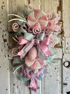 a pink and green wreath hanging on the side of a wooden door with ribbons around it