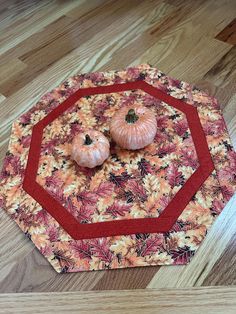 two small pumpkins sitting on top of an orange and red piece of cloth in the shape of a octagon