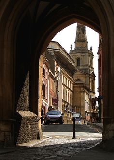 an archway leading to a building with a clock tower in the background and cars parked on the street below