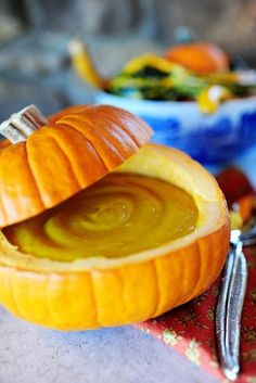 a carved pumpkin sitting on top of a table next to a fork and bowl filled with soup