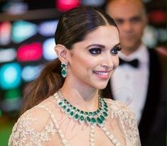 a woman in a white dress with green jewels on her neck and wearing an emerald necklace