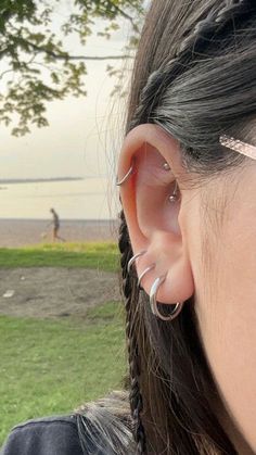 a woman with ear piercings on her ears looking at the grass and water in the distance