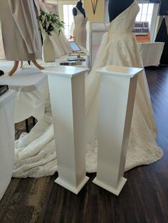 two tall white pedestals are on display in a bridal gown shop, with mannequins behind them