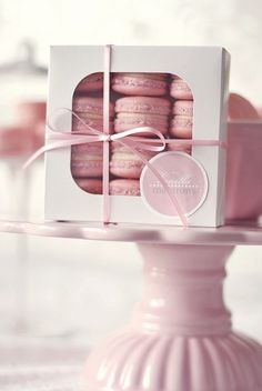 a box of pink macaroons sitting on top of a cake stand