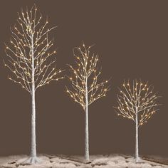 three white trees with lights on them in the snow