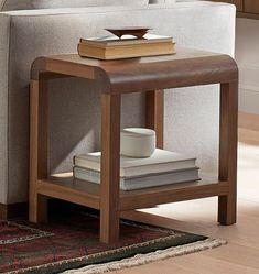 a coffee table with books and a cup on it in front of a couch next to a rug