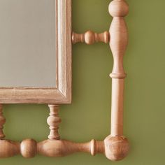 a mirror on the wall next to a wooden rod and ball finial with a green painted wall in the background