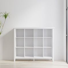 an empty white bookcase next to a potted plant