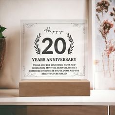 a glass sign that reads twenty years anniversary on the side of a shelf next to a potted plant