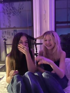 two women sitting on a bed and one is holding her face up to the camera