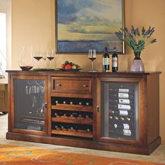 a wooden buffet table with wine glasses and bottles on the top, in front of a painting