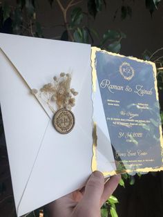 a person holding up an envelope with a wax stamp on it and some flowers in the middle