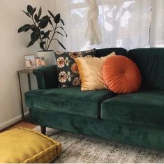 a green couch with orange pillows in front of a window